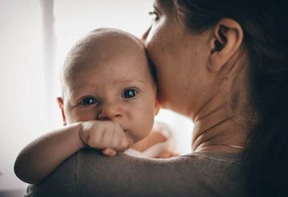 Ein Baby schaut über die Schulter seiner Mutter.